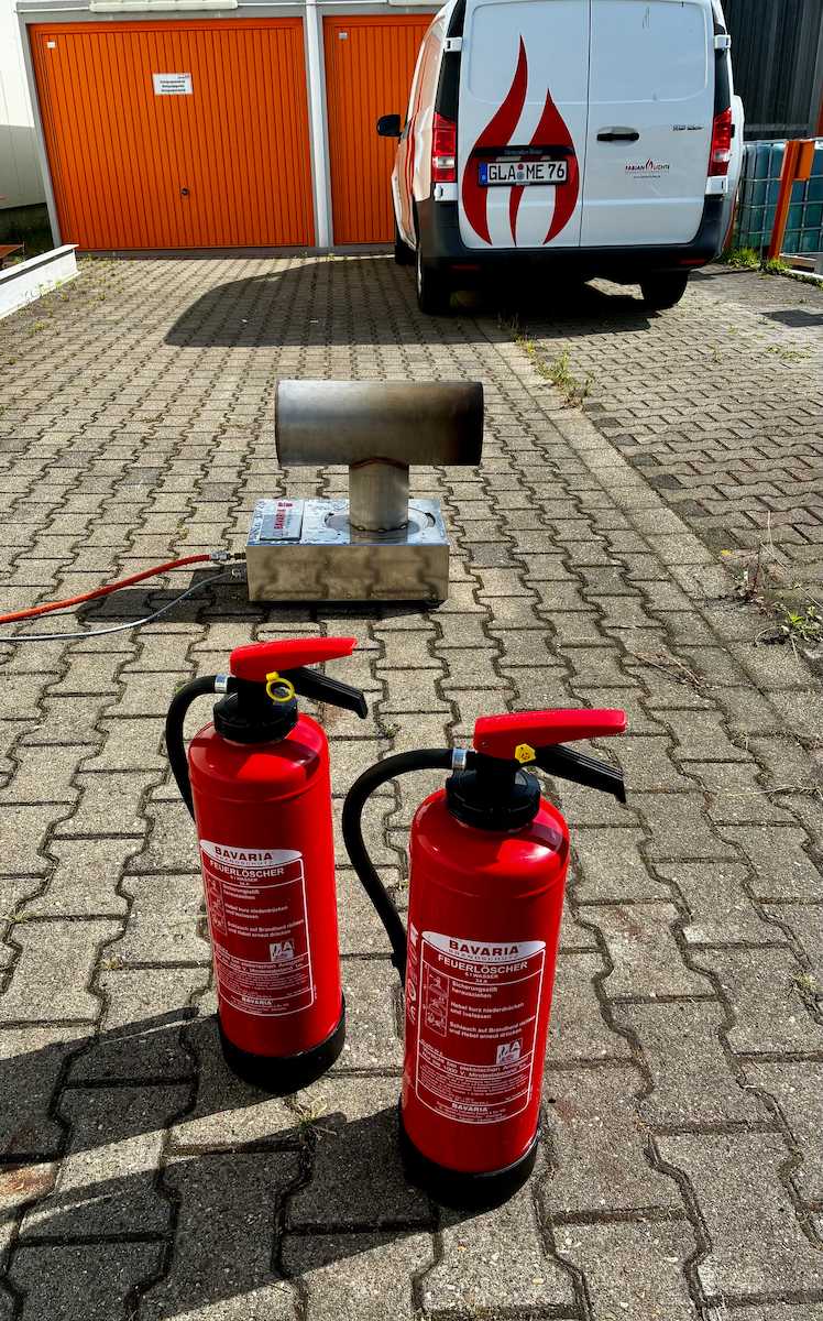 Zwei Feuerlöscher und ein Gasbrenner stehen in einem Hof. Dahinter ein Fahrzeug von Fabian Lichte - Brandschutzberatung